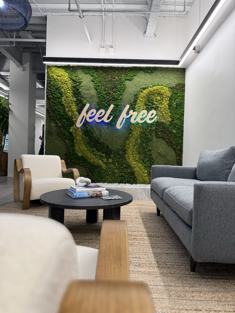 Preserved moss wall with a neon 'feel free' script logo behind a styled office lounge